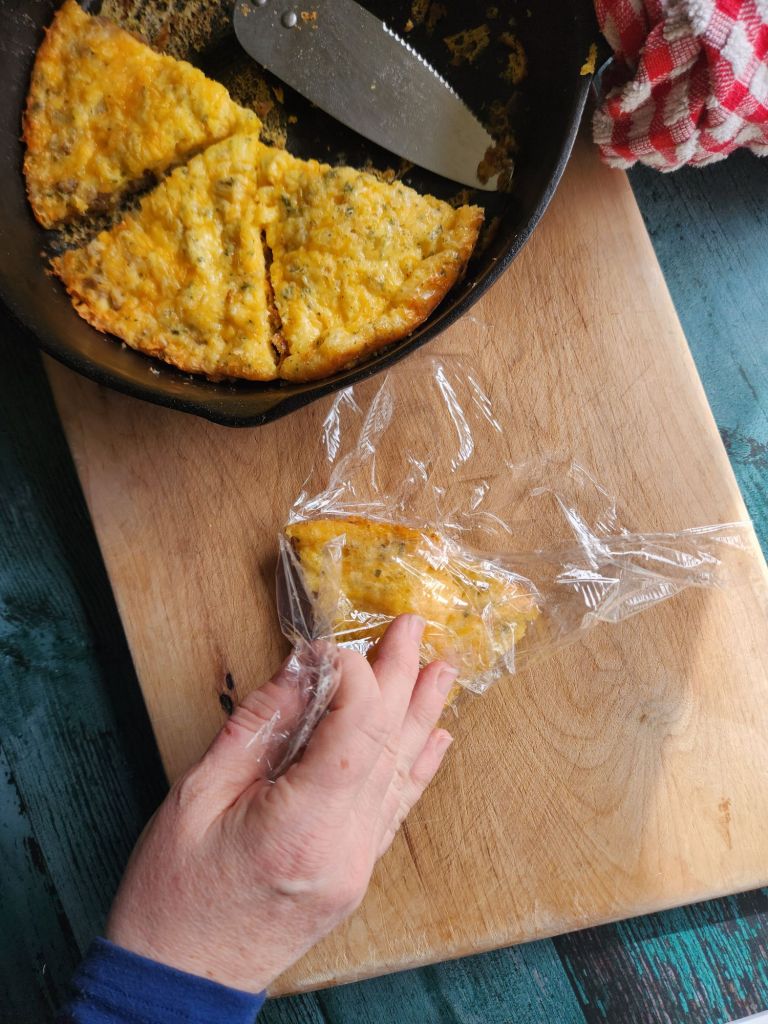 Wrapping a piece of low carb sausage and cheese frittata with plastic wrap to freeze.