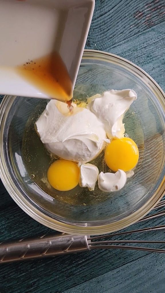Adding vanilla extract to bowl with sour cream and eggs for egg mixture in Grandma's gluten free cinnamon coffee cake recipe.