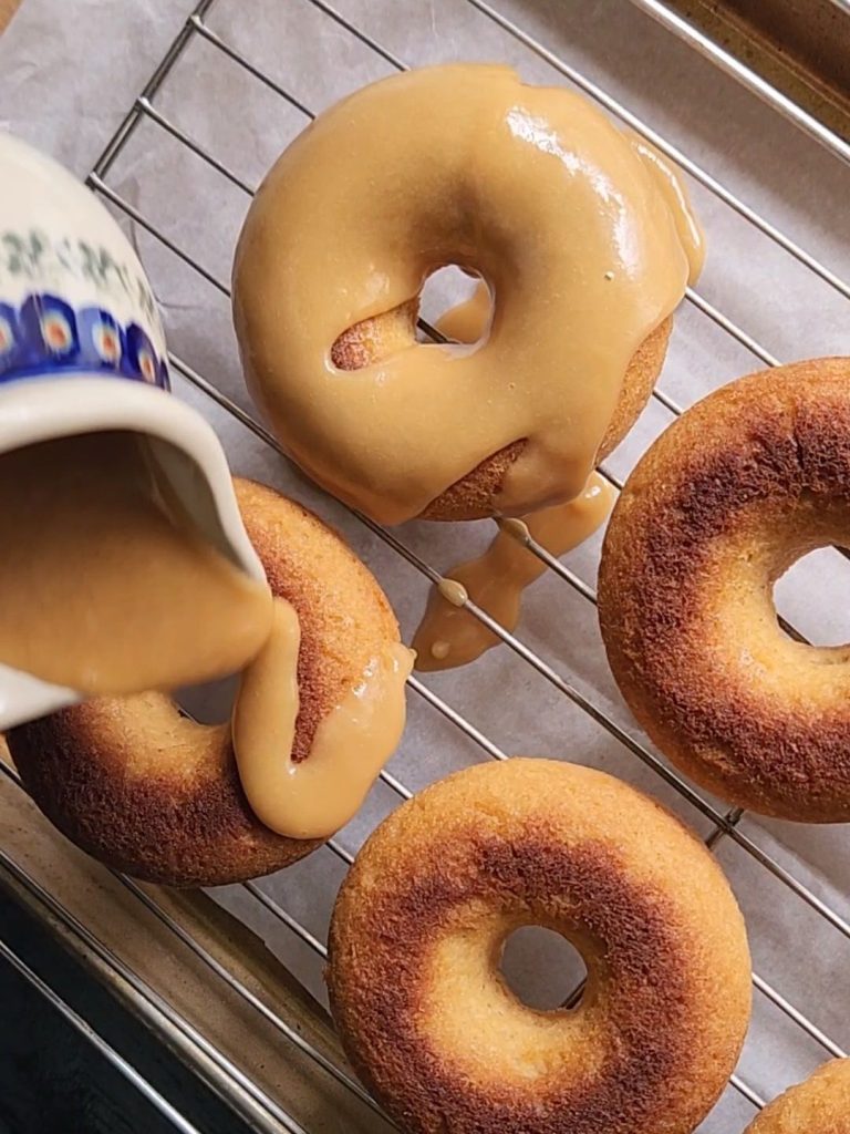 Keto maple glaze being poured over gluten-free maple donuts.