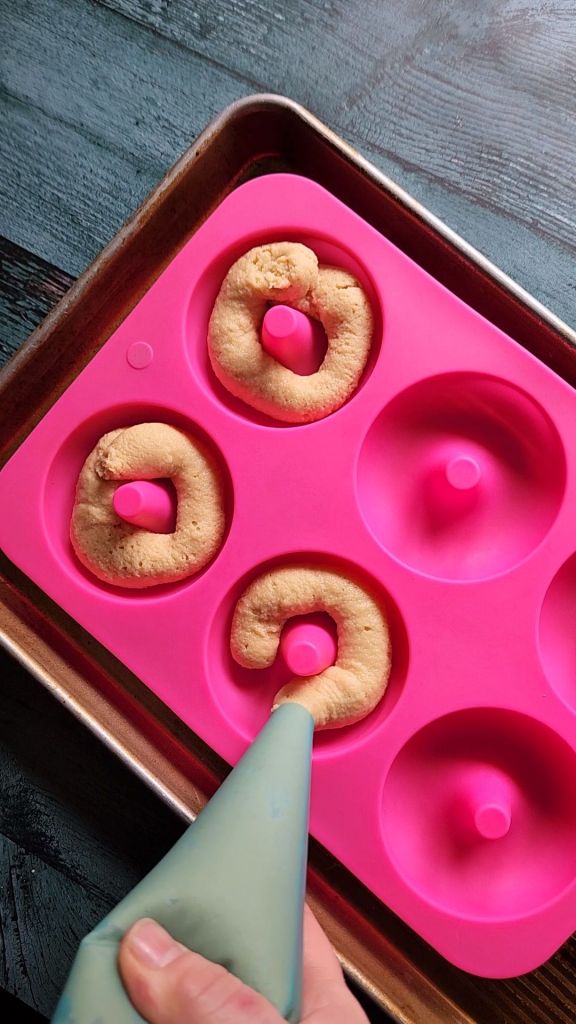 Piping batter for gluten-free Maple Donuts into a silicone donut pan.