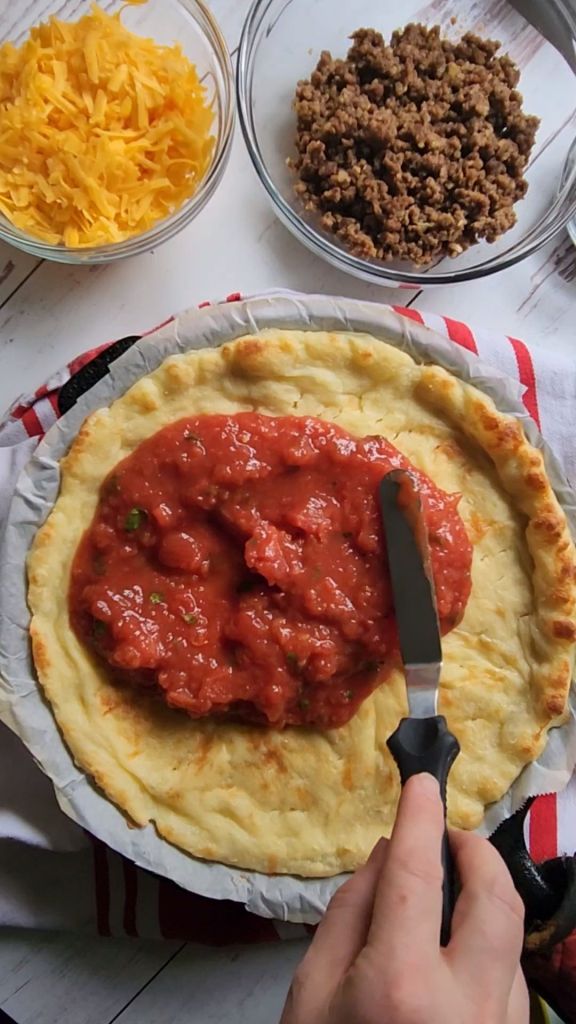Spreading salsa on gluten-free 10-in par baked crust.