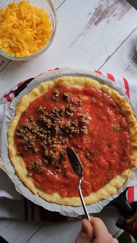 Sprinkling prepared taco meat over salsa layer for gluten-free copycat Godfather's taco pizza.