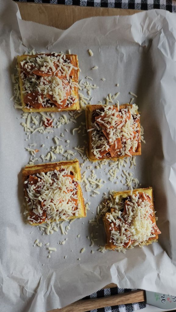 Easy gluten free keto mini pizza chaffles topped with pizza toppings and being put into the oven to bake.