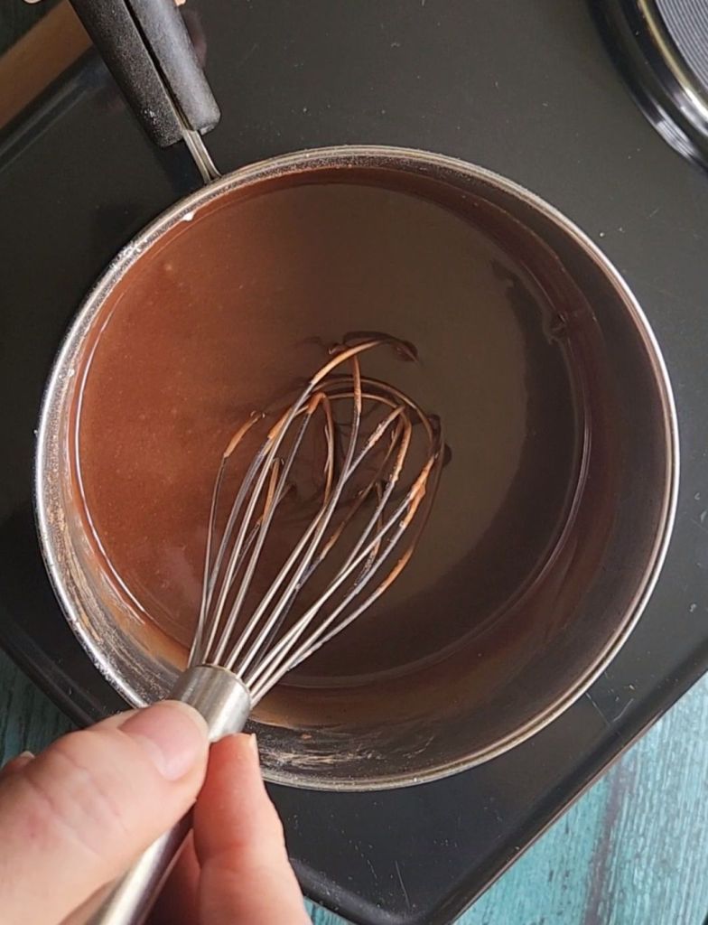 Chocolate glaze for gluten-free Baileys Irish Cream chocolate bundt cake being stirred in a saucepan.