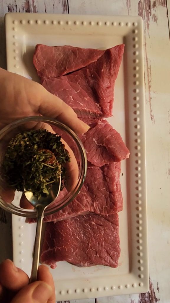Mixing seasoning rub on round steaks to make easy gluten-free copycat McCormick Swiss steak recipe.