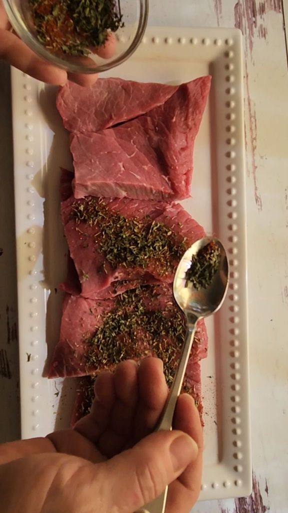 Sprinkling seasoning rub on round steaks to make easy gluten-free copycat McCormick Swiss steak recipe.
