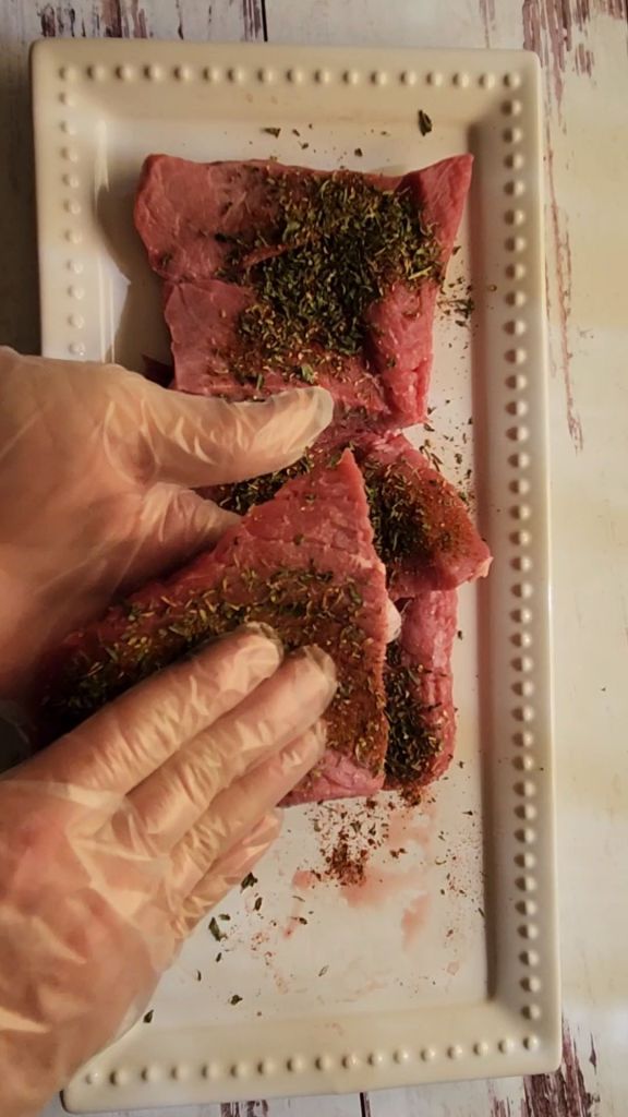 Rubbing seasoning on round steaks to make easy gluten-free copycat McCormick Swiss steak recipe.