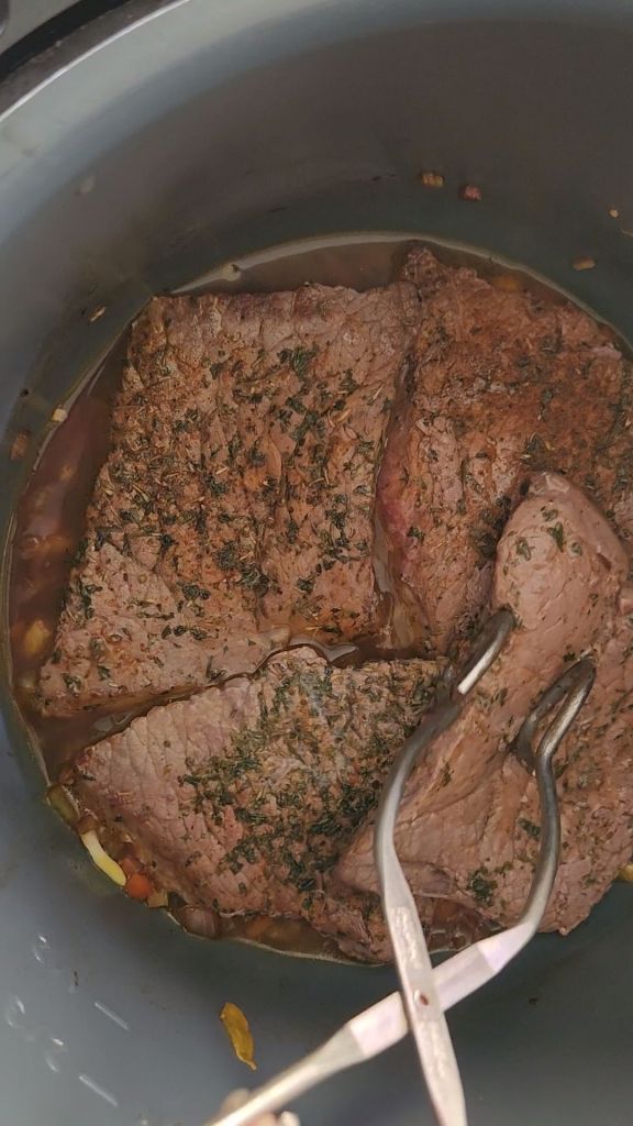 Placing seared round steaks into instant pot on top of sauteed veggies.
