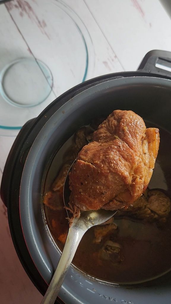 Lifting cooked pork put of the broth for Easy instant pot carnitas from a pork shoulder roast.