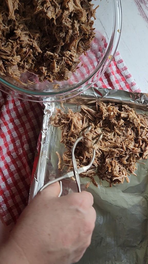 Placing shredded pork on baking sheet to crisp in the oven for Easy instant pot carnitas from a pork shoulder roast.