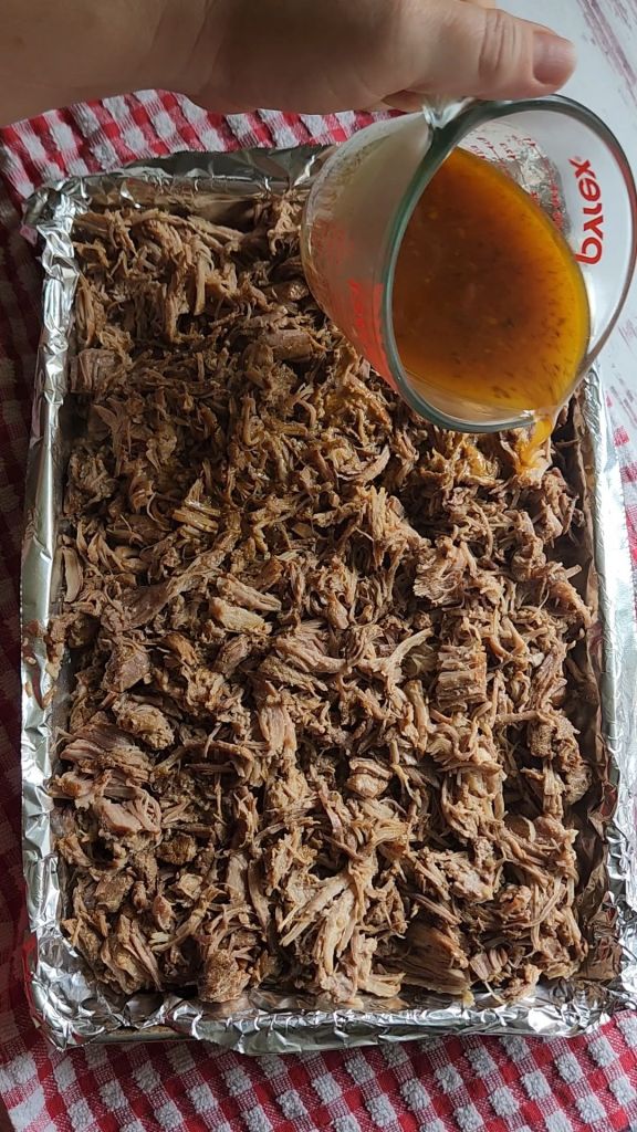 Pouring spiced broth over shredded pork roast for Easy instant pot carnitas from a pork shoulder roast.