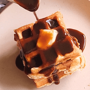Pouring Maple syrup over Easy gluten free low carb breakfast chaffle waffles batter into waffle maker.