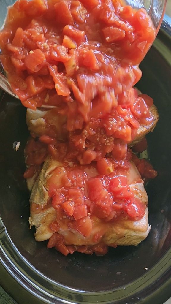 Pouring diced tomatoes and garlic over pork loin roast in crock pot.