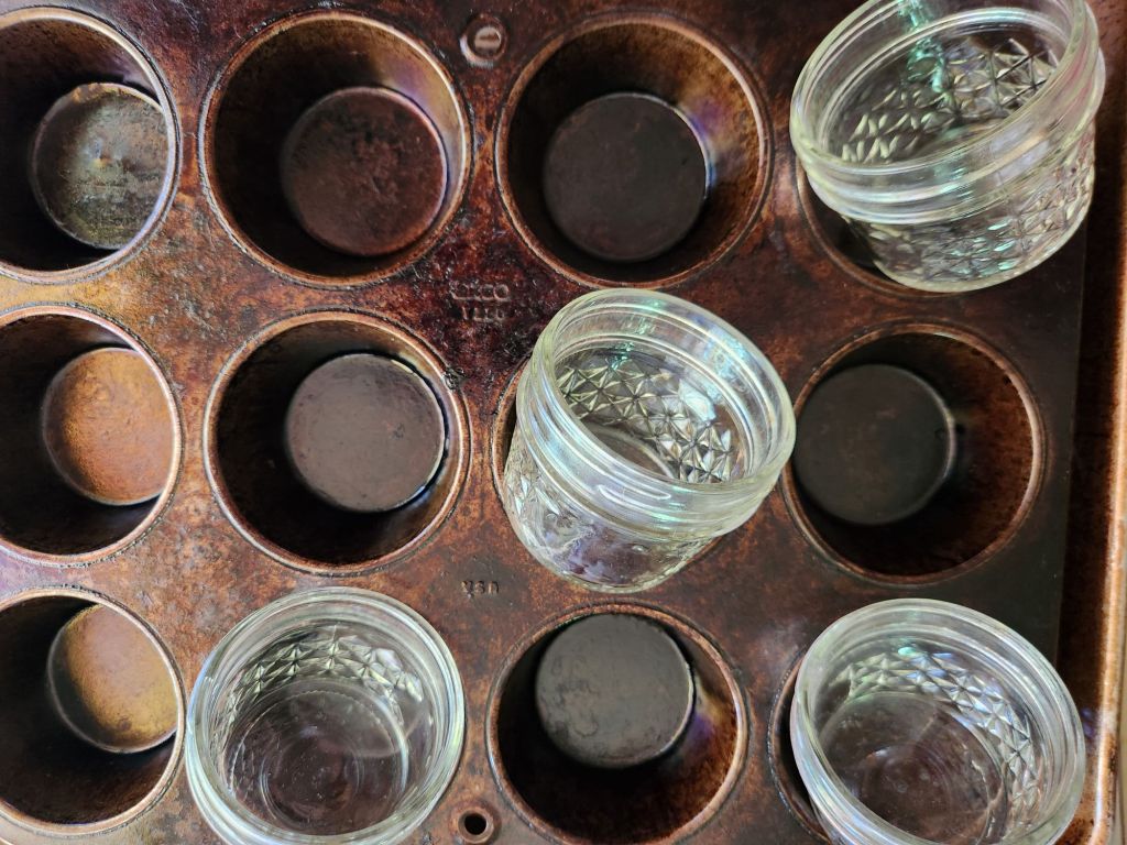Empty 4oz mason jars tilted in muffin pan.