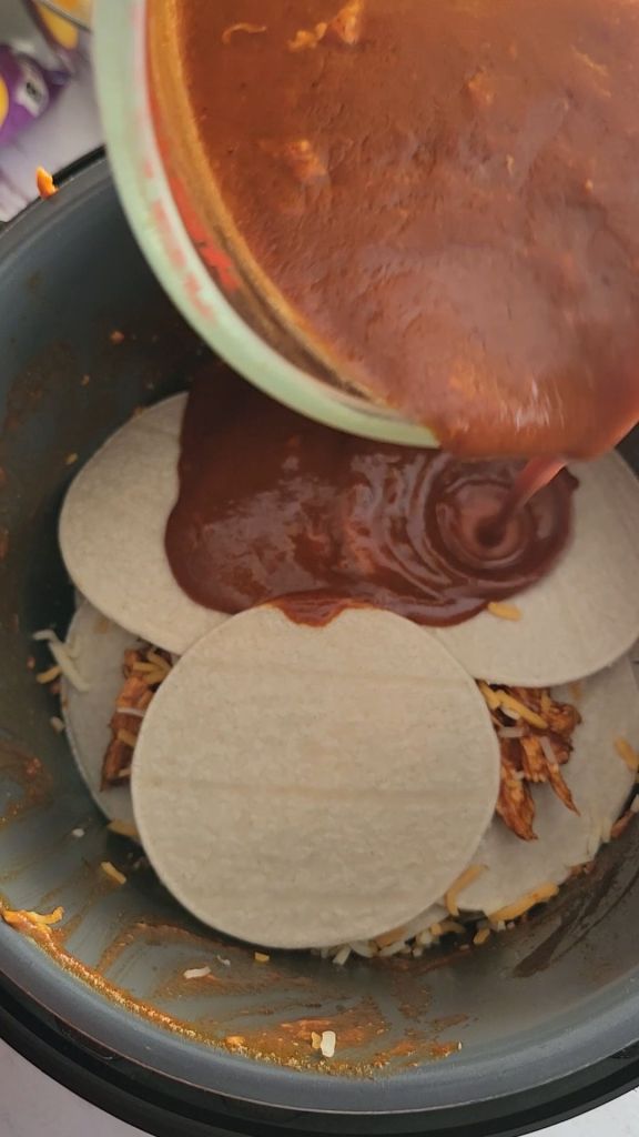 Pouring final enchilada sauce over last tortilla for Easy instapot gluten free mexican casserole recipe.