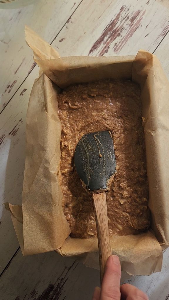 Spreading batter from Easy gluten free zucchini bread with yellow squash recipe into parchment lined pan.