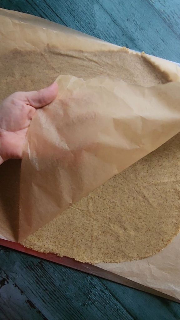 Peeling off parchment paper on baking sheet to roll out Gluten-Free Nut Free Sunflower Seed Crackers Recipe.
