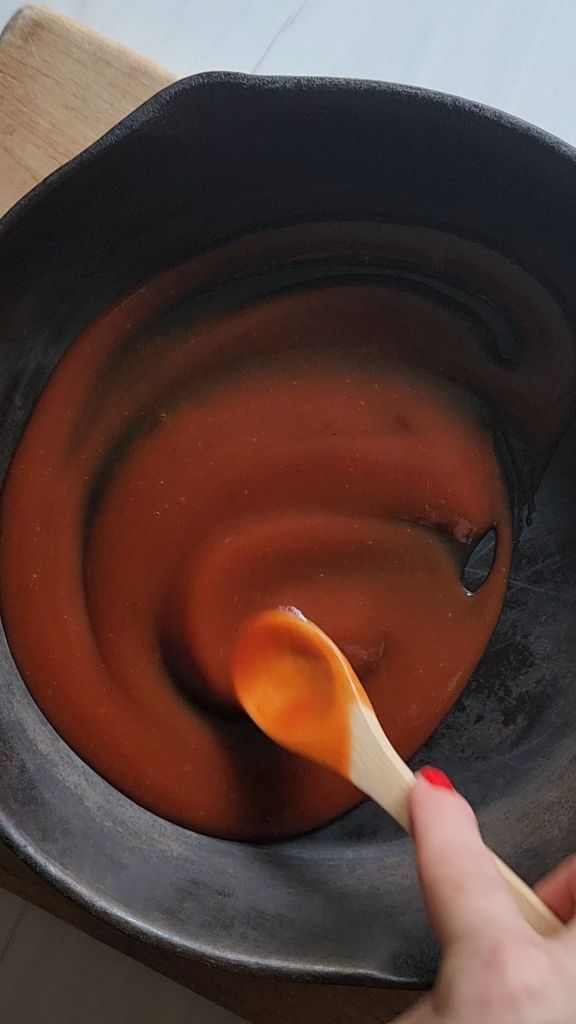 Spreading sauce in the bottom of the skillet for Easy Gluten Free BBQ Skillet Hamburger Steak Recipe.