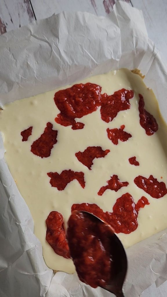 Swirling strawberry into batter for Gluten free low carb strawberry lemon cheesecake bars.
