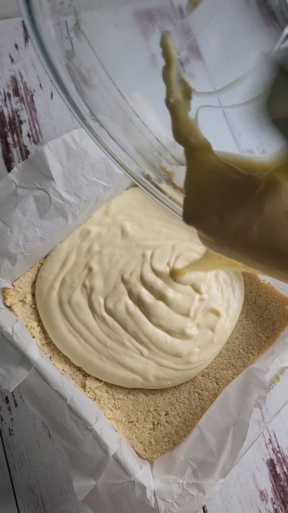 Pouring cheesecake batter onto parbaked crust.