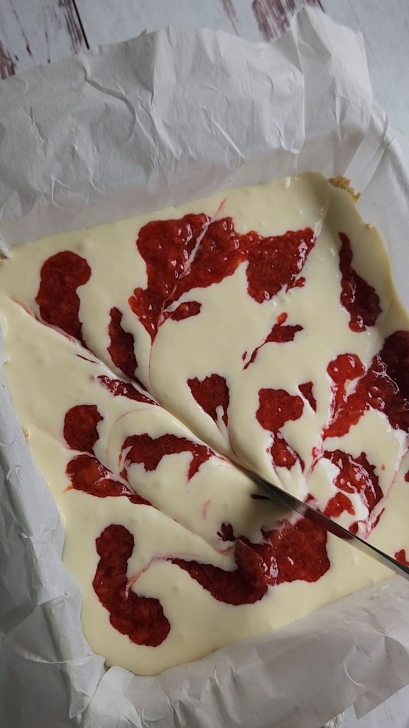 Swirling strawberry into batter for Gluten free low carb strawberry lemon cheesecake bars.