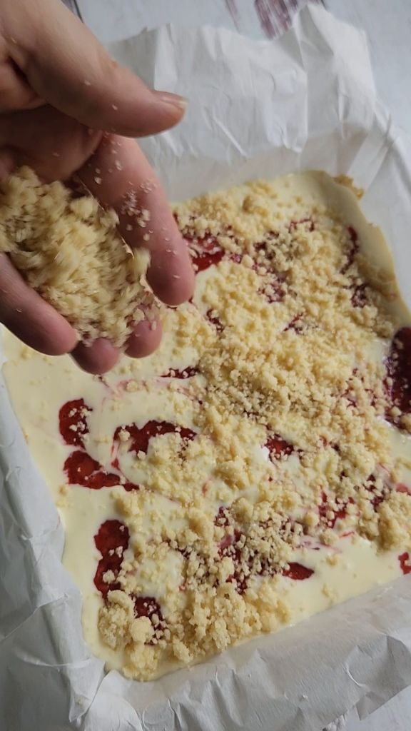 Sprinkling reserved crumbs on top for Gluten free low carb strawberry lemon cheesecake bars.